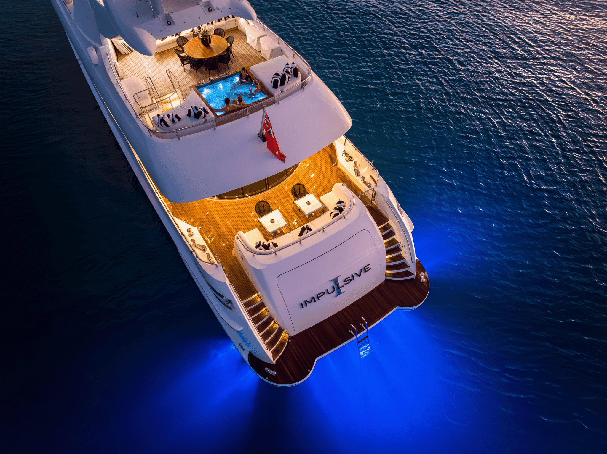 The motor yacht Impulsive at dusk from the air, underwater lights glowing
